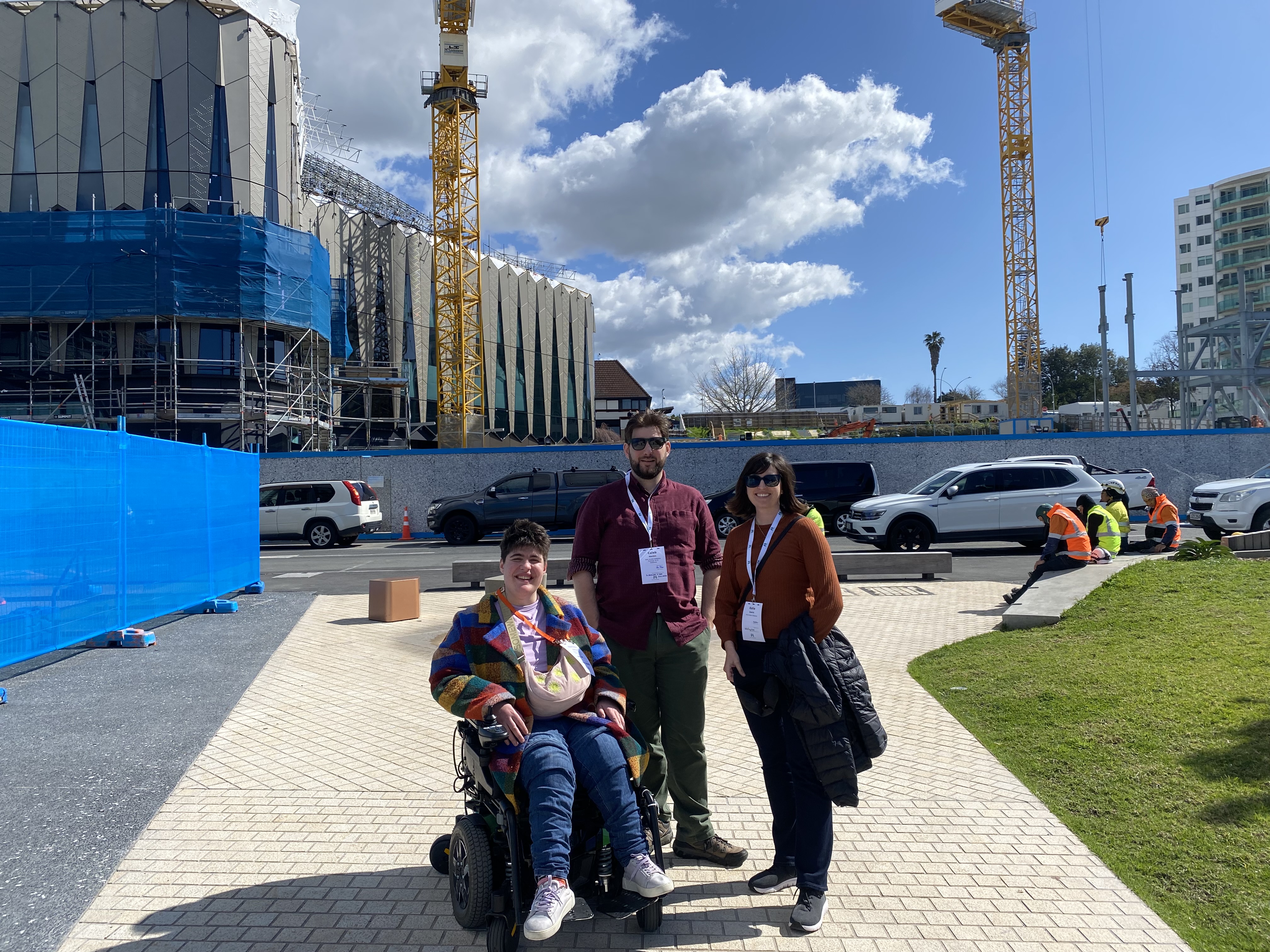 From left to right, Henrietta Bollinger, Caleb Gordon, and Katie Querin gather together for a photo in front of the construction site of the Tauranga Museum building